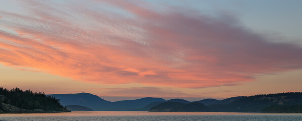 Fototapeta na wymiar Sunset makes the clouds glow pink over the San Juan Islands as seen from Hunter Bay on Lopez Island.