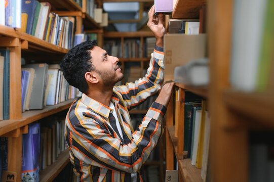 Male indian student at the library with book