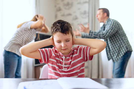 Sad child covers his ears with his hands during an argument between his parents