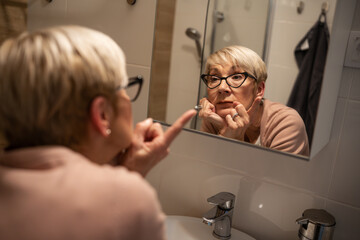 Confident senior woman looking at her reflection in the mirror and talk to himself. Trying to rise self-esteem and motivate himself.	
