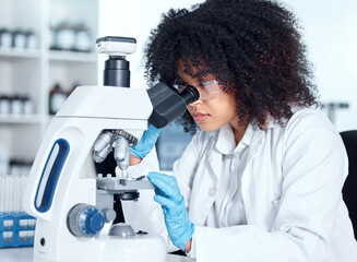 Young african american woman wearing a labcoat and goggles looking at medical samples on a microscope in her lab. A mixed race female scientist wearing goggles and gloves conducting research - Powered by Adobe