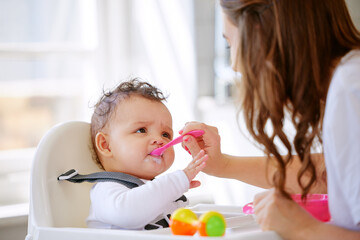 Eat up little one. Shot an attractive young woman sitting in the kitchen with her daughter and feeding her.