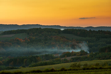 sunset colors over forests and fields, smoke over trees - obrazy, fototapety, plakaty
