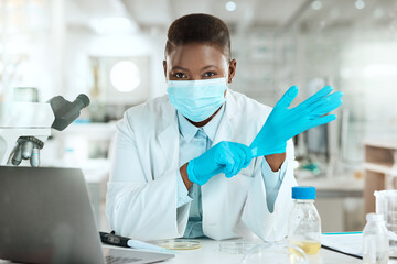 Im ready to work with samples. Shot of a young scientist sitting alone in her laboratory and putting surgical gloves on.