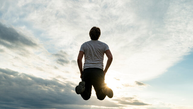 Low angle view of a man jumping up high in the air under a dramatic sky
