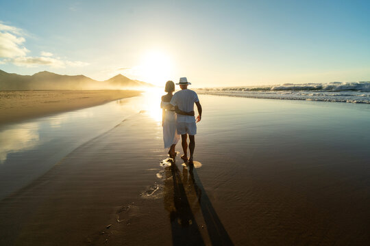 Back view of romantic couple walks along a sandy beach on the Fuerteventura island.