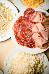 Mix of different snacks and appetizers on white plates. Sausage, cheese, jamon.