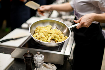 Woman cooking potatoes cut into squares in steel pan on kitchen