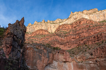 Fototapeta na wymiar Scenic view on a massiv cliff seen from Bright Angel hiking trail at South Rim of Grand Canyon National Park, Arizona, USA. Light shining on steep stone wall and rock formations with blue sky