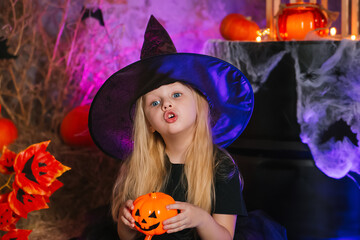 A little girl with blond hair in a black dress and a witch hat for Halloween.