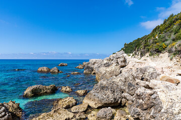 A beautiful landscape of the coast of the island of Corfu in the Ionian Sea of the Mediterranean in Greece. Pure blue clear water washes over the shores of the Greek island.