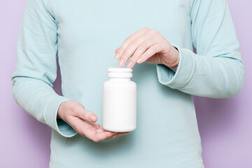 White plastic bottle in female hand. Packaging for pills, capsules or supplements.