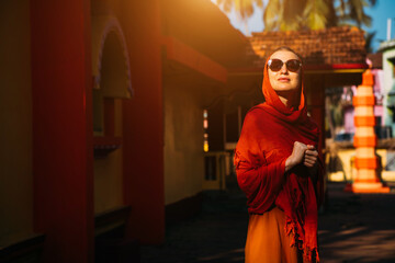 A beautiful European tourist girl admires a Hindu temple on a trip to India. Harmonious yellow and red combination of clothing, architecture and sunlight