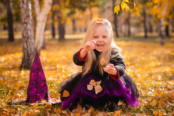 A little girl with blond hair in a black dress and a hat in the image of a witch for Halloween in...