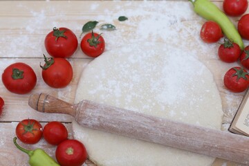 Raw dough, yeast for pizza, rolling pin, tomatoes, chili pepper, flour, book with recipes, wooden background, on the table, photo background