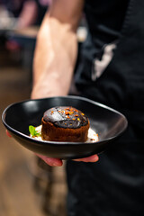 waiter hand hold Basque cheesecake with Chocolate and cream in bowl