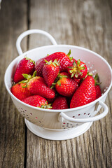 Strawberries in white colander placed on a rustic wooden background. Fresh and tasty seasonal ripe and fruit.