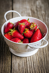 Strawberries in white colander placed on a rustic wooden background. Fresh and tasty seasonal ripe and fruit.