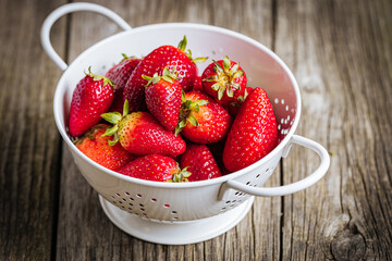 Strawberries in white colander placed on a rustic wooden background. Fresh and tasty seasonal ripe...