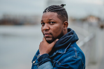 A black young man with dreadlocks in a blue denim jacket and sweatpants is standing on the...