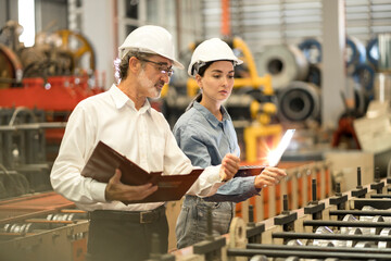 two professional engineer,worker,technician use clipboard discuss work, walk in steel metal manufacture factory plant industry. Black African American man and woman wear hard hat check quality machine