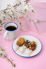 cake pops on a blue rimmed plate and a cup of coffee and round shaped gift box on pink background