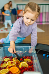 Little girl playing in handmade fruit bar with kitchenware, berries and citrus fruits. Sensory development and experiences, themed activities with children, fine motor skills development