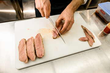 Close-up photo of a chef hands slicing baked meat on a kitchen board