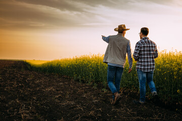 Two farmers walking on a farmland at unset and talking. - obrazy, fototapety, plakaty