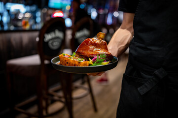 Waiter hold plate with Roasted pork knuckle in restaurant