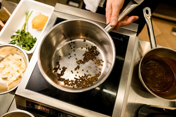 Man's hand holding steel stewpan standing on kitchen scales. Chief cooking spices in stewpan.