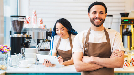 Smiling barista holding his arms crossed and standing in coffee shop