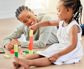 Obraz na płótnie Canvas African american girl playing with building blocks while sitting with mother. Little girl building tower with wooden blocks. Smiling woman lying on the floor and playing with child