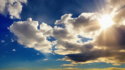Obraz premium The sun is shining from behind the clouds in the blue sky. Bright sun rays shine on the clouds. Generated by AI. International Sun Day.