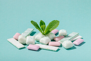 A bunch of mint and fruit chewing gum and fresh mint leaves on a blue background