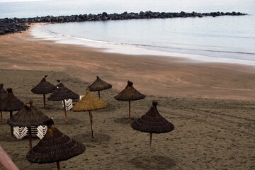 Straw beach umbrellas and folded empty deckchairs on one of the beaches of Tenerife
