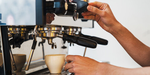 Barista making coffee with espresso machine while holding cup