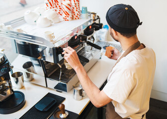 Male barista preparing coffee at espresso machine in coffee shop