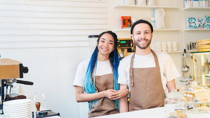 Happy two employees working in coffee shop while posing at camera