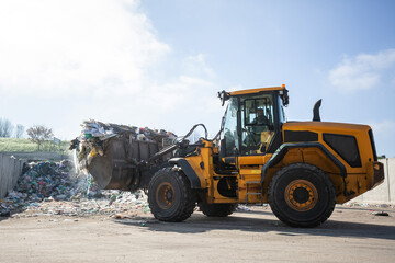 Yellow skid steer loader moving wooden waste material, shaking out a scrap grapple on the garbage heap in the materials recovery facility
