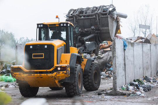 Yellow skid steer loader moving wooden waste material, shaking out a scrap grapple on the garbage heap in the materials recovery facility
