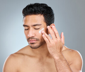 Obraz premium Theres nothing wrong with taking care of yourself. Shot of a man applying moisturiser to his face while standing against a grey background.