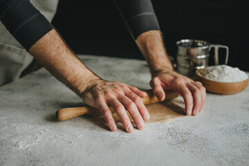 Unrecognizable man rolling out the dough with a rolling pin on black background