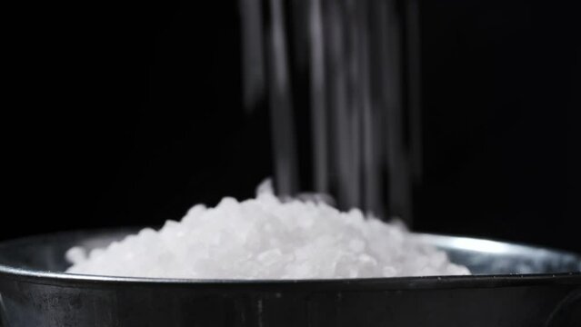 Pouring coarse white salt in a metal bowl on the black background. Close up shot