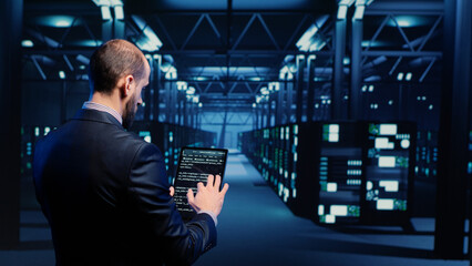 Fototapeta premium Datacenter engineer inspecting working server computers with web information on tablet, future digitalization. Modern IT administrator running diagnostics on networking connection. Tripod shot.