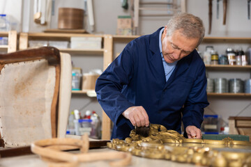 Employee of the restoration workshop treats the wooden frame of vintage mirror with a protective...