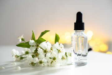 Clear glass cosmetic dropper bottle and white cherry flowers with bokeh lights, care product mockup