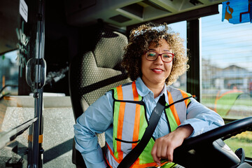 Happy mid adult woman driving bus and looking at camera.