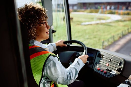 Female bus driver behind steering wheel.