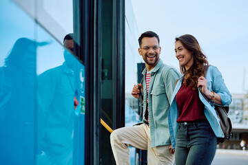 Cheerful couple boarding in public transport at bus station.